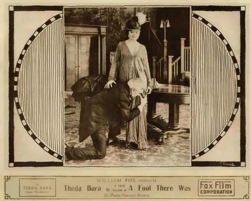 Promotional photo for the 1915 film “A Fool There Was” features Theda Bara and costar Edward Jose. She stands in a well-appointed drawing room and gazes down triumphantly at Jose, who kneels at her feet and clasps his arms around her knees like a child.