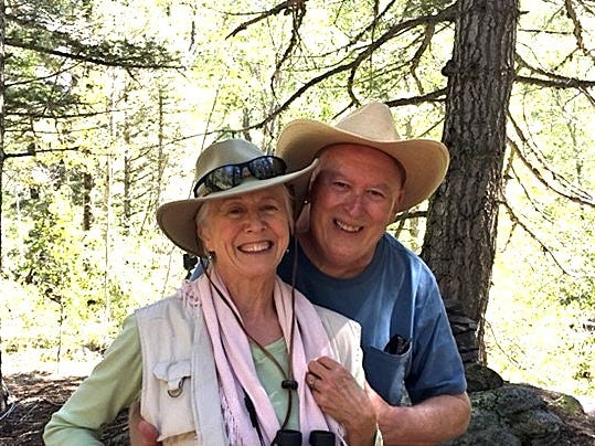 photo of a man and woman amidst green trees. The man has his arms around the woman and they are both laughing