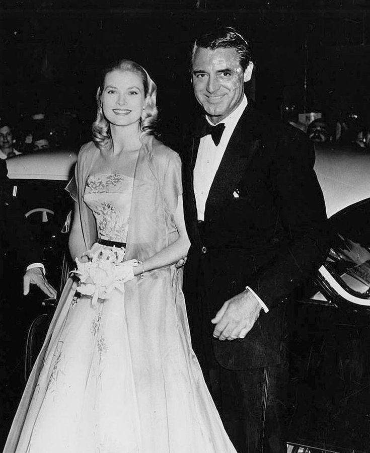 This may contain: an old black and white photo of two people in formal wear standing next to a car This may contain: an old black and white photo of two people in formal wear standing next to a car