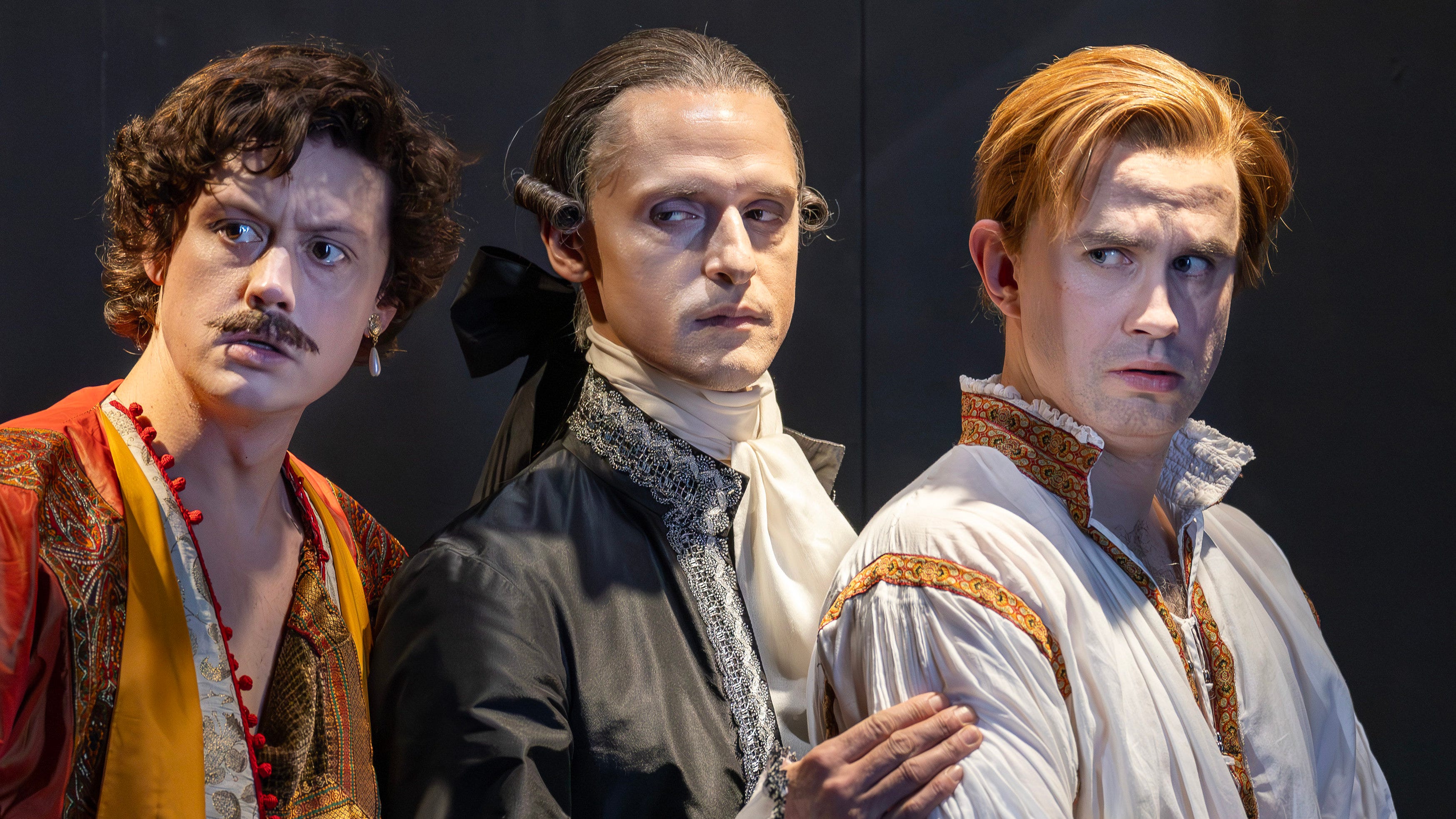 Three men in 18th century dress stand in a row, glowering and giving side-eye. Their faces are powdered but two are in 'exotic' orientalist dress. Three men in 18th century dress stand in a row, glowering and giving side-eye. Their faces are powdered but two are in 'exotic' orientalist dress.