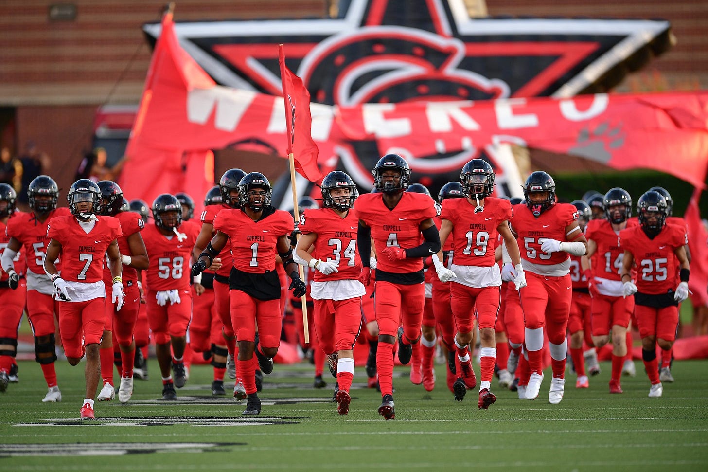 A group of football players in red uniforms run onto a field
