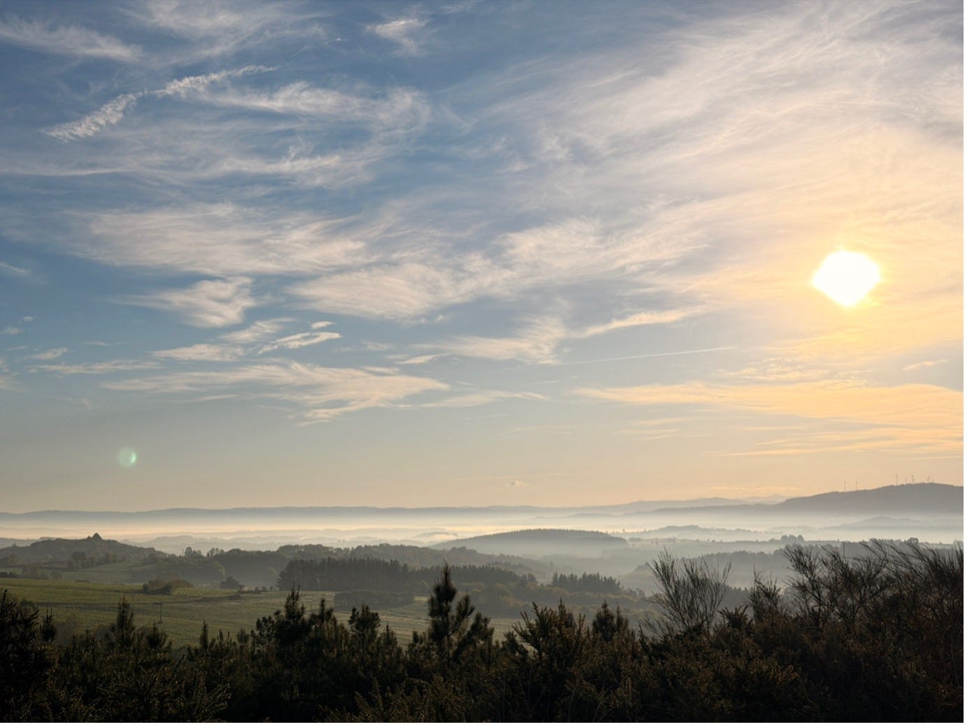 A different view of sunrise overlooking a green and hilly landscape.