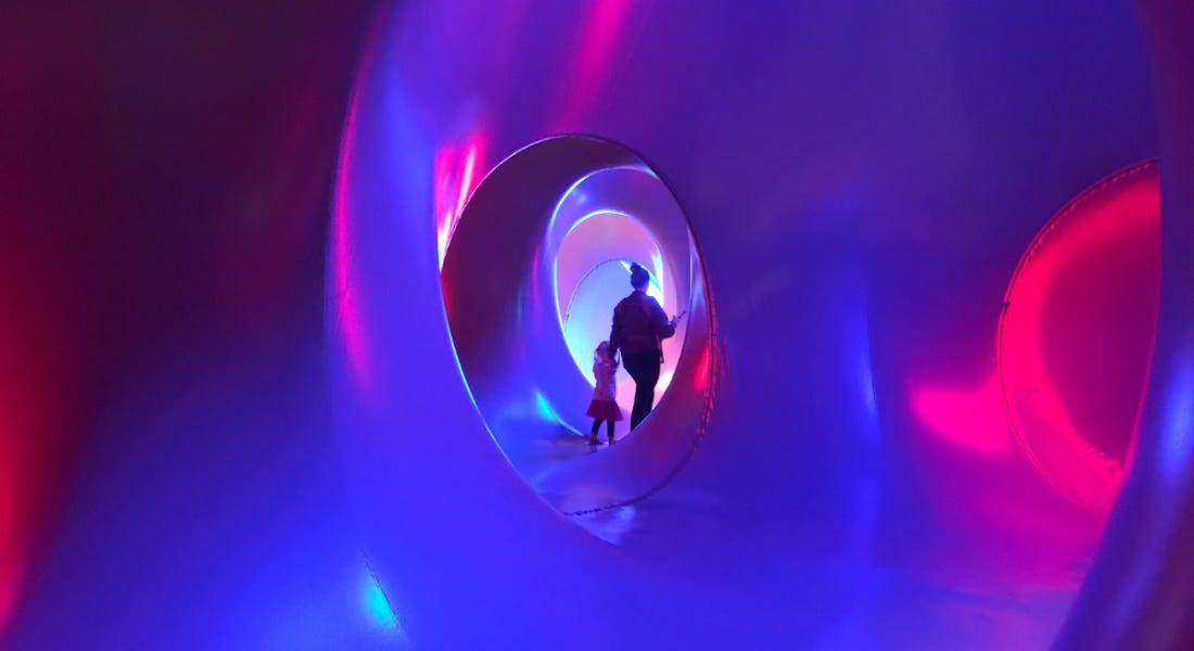 The interior of an inflatable structure with purple colours inside of it, and a woman and child walking in the distance