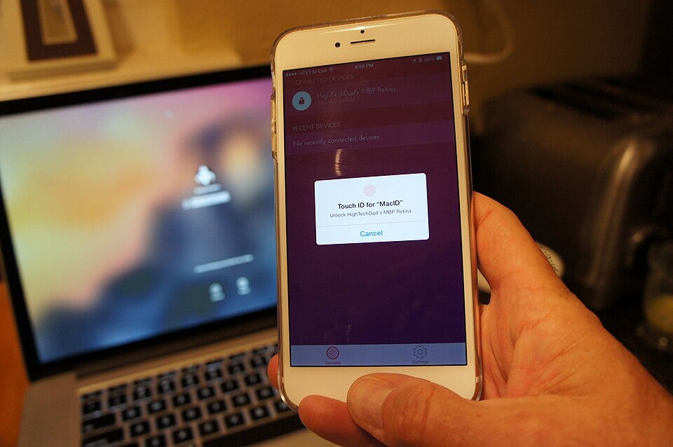 A photo of a person using an iPhone to unlock a MacBook Pro with MacID. A photo of a person using an iPhone to unlock a MacBook Pro with MacID.