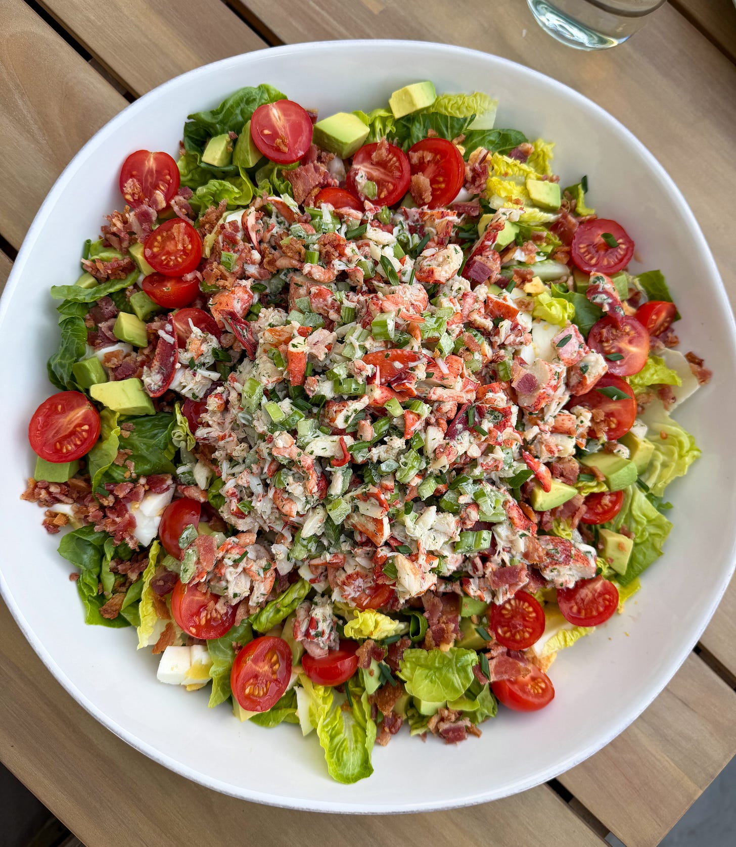 A vibrant and delicious Lobster Cobb Salad in a large serving bowl in an al fresco dining setup.