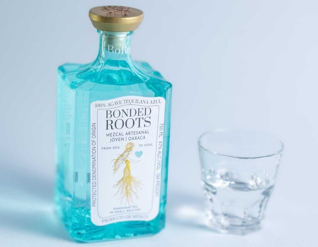 Bonded Roots Mezcal bottle with a glass of mezcal on a light background.