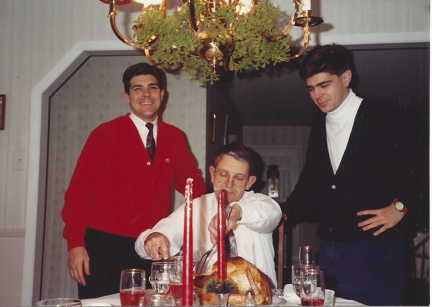 Father carves the turkey while his two young adult sons stand beside him