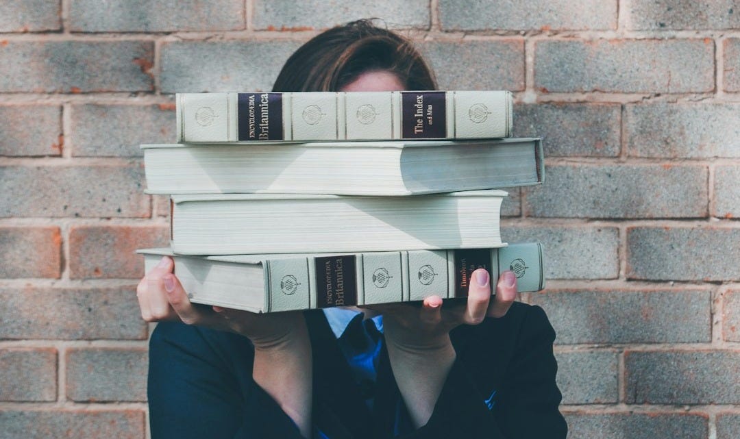 person holding pile of books near face person holding pile of books near face