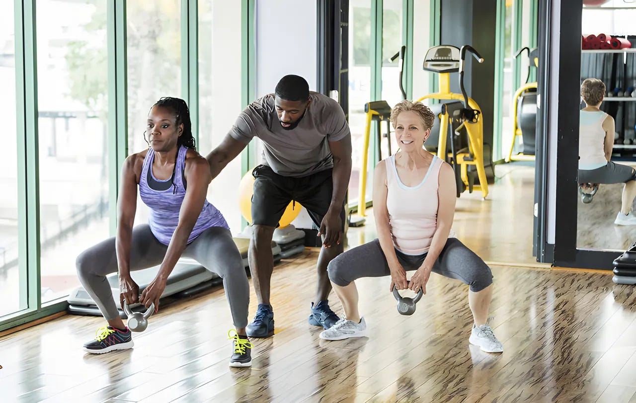 Two women in the gym working out with kettlebells with a personal trainer.