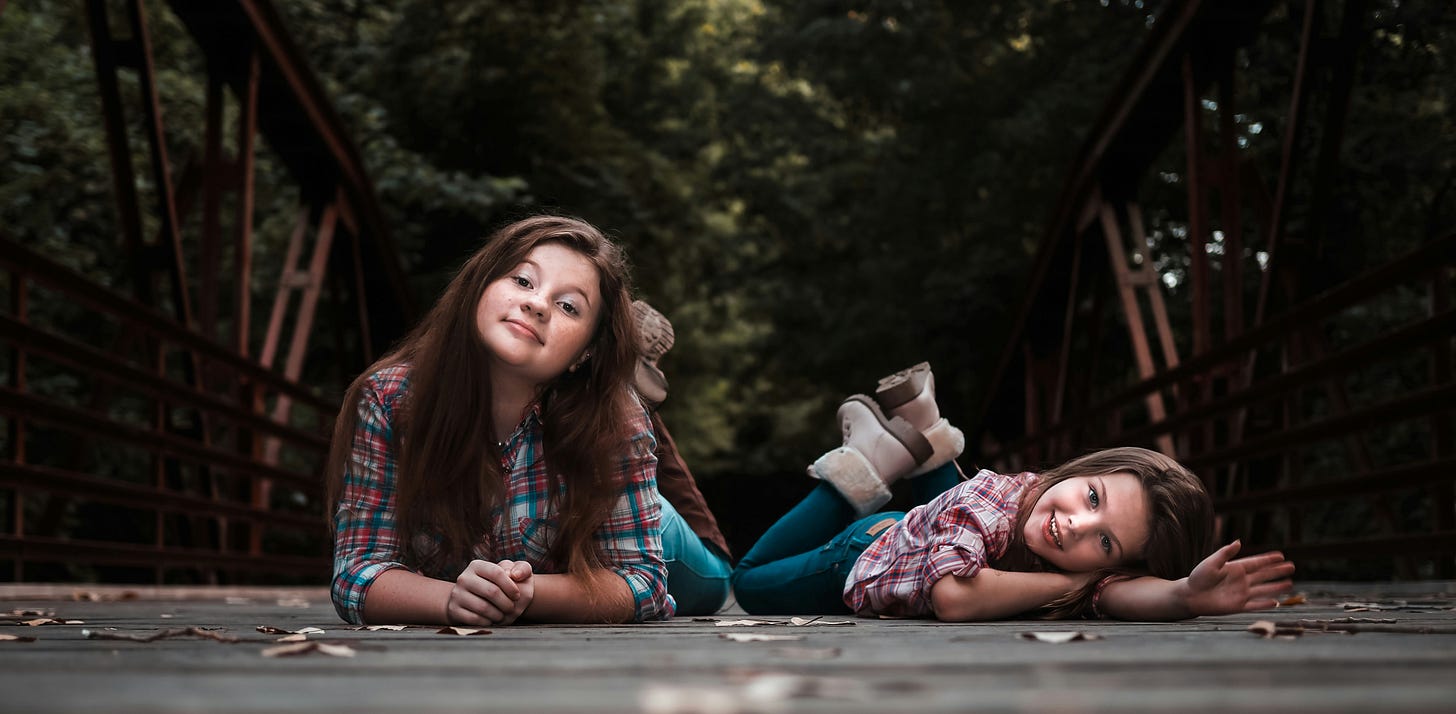 little girls sisters lying on ground in matching shirts and jeans