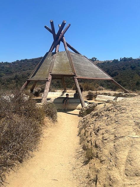 Photos of a desert hike featuring pictures of brown landscape, a waterfall, the author, a teepee, and a fence post with a quote on it.