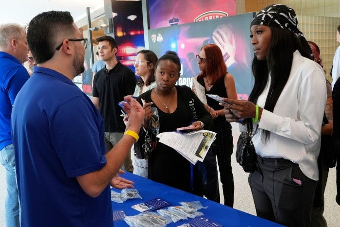 Logan Reed, left, talks with job seekers at a table during a job fair, with several people listening and holding resumes.