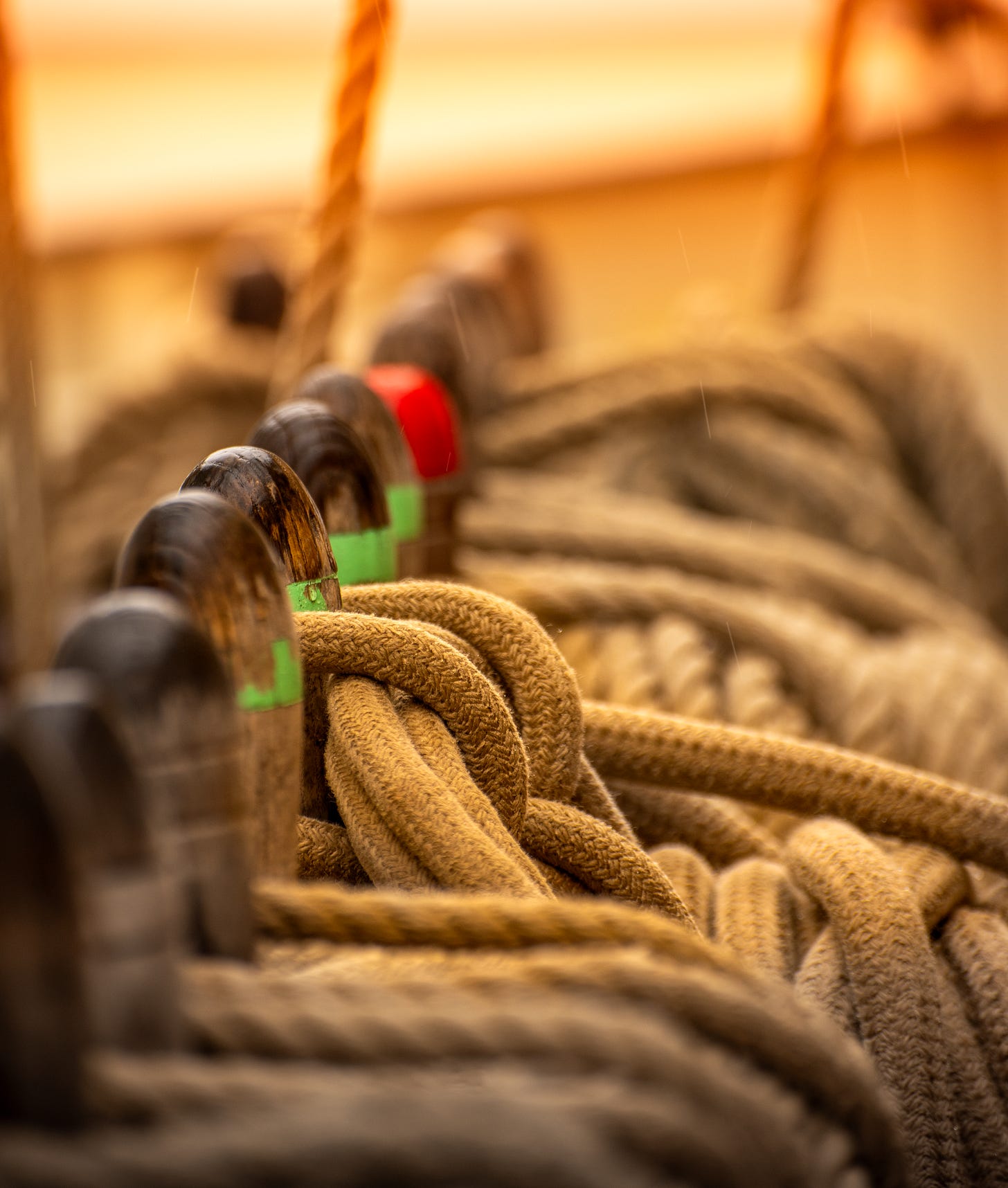 A close-up photograph of thick, coiled ropes neatly arranged on a wooden ship railing, secured around wooden belaying pins. The warm golden lighting creates a sense of nostalgia and craftsmanship, highlighting the texture of the ropes and the worn wood. The scene evokes themes of structure, connection, and tension—symbolic of communication, trust, and the ways in which conversations can either secure or constrain relationships.