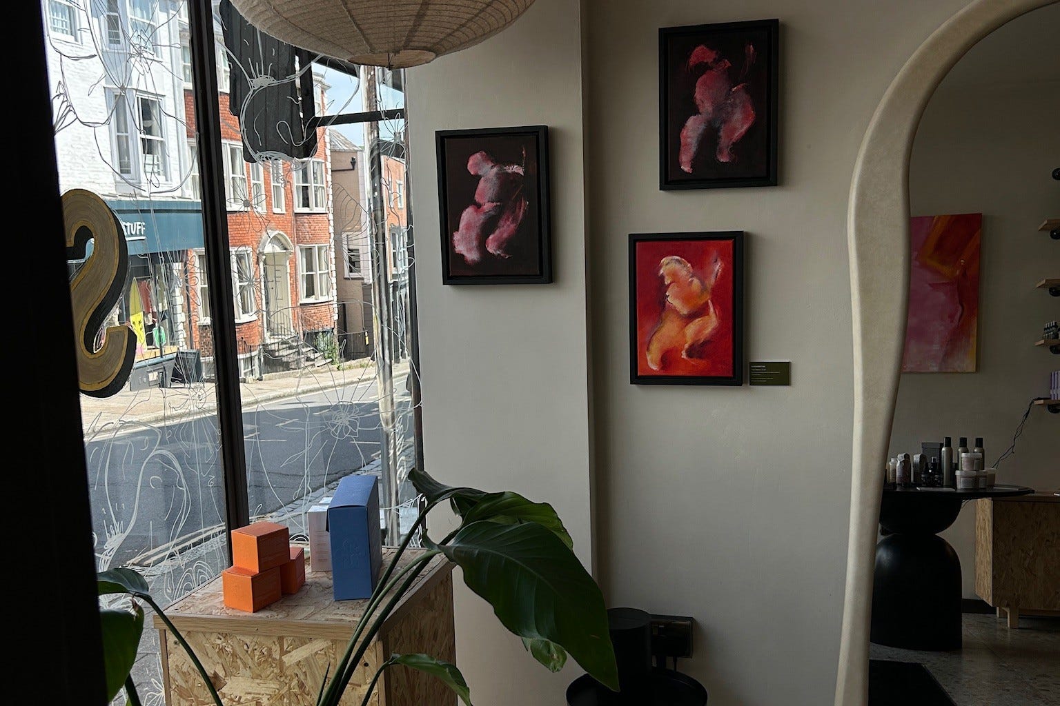 Framed paintings and an arched doorway inside SHY, with the street outside visible through the window