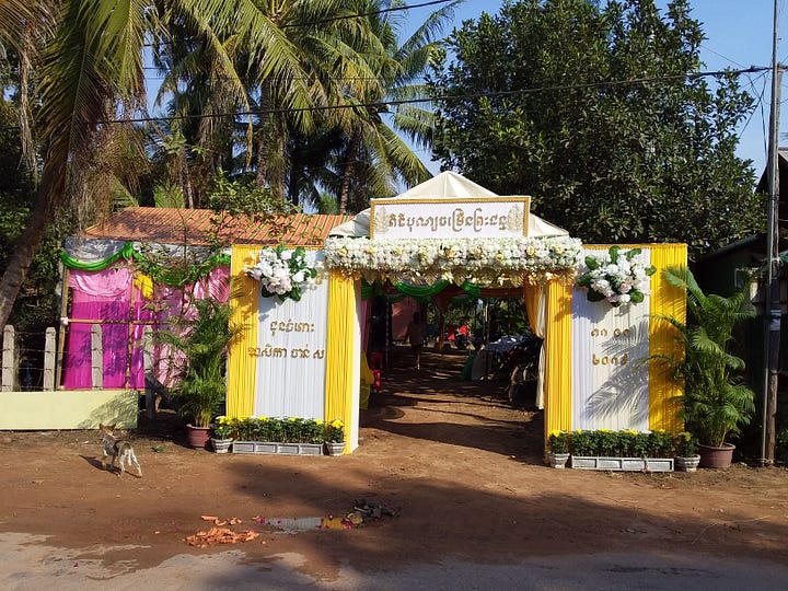 A side-by-side image. The left side shows a digital Google Maps screenshot highlighting a driving route from Siem Reap heading north toward Banteay Srei. The right side is a photograph of a traditional Cambodian celebration tent erected on a dirt road. The tent entrance is elaborately decorated with bright yellow and white draped fabrics and floral arrangements, set against a backdrop of lush green palm trees.