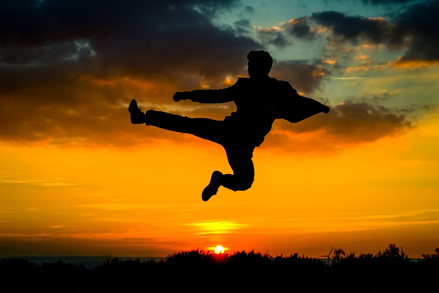 Outline of man fly kicking mid-air above a sun set