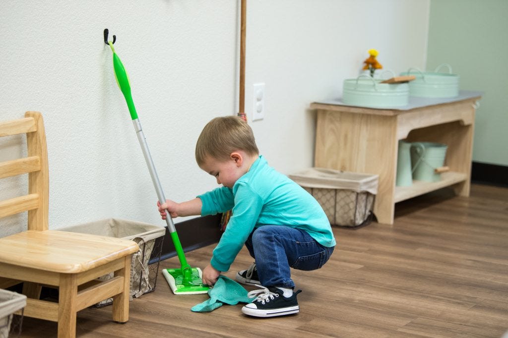 Child cleaning the classroom floor with a mop during practical life work in the Guidepost Montessori experience Child cleaning the classroom floor with a mop during practical life work in the Guidepost Montessori experience