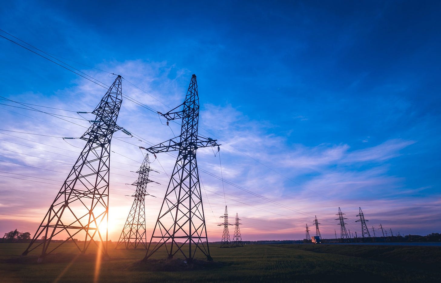 Electricity pylons and power lines crossing open fields at sunset