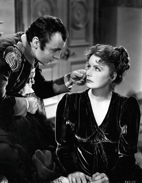 Napoleon, standing, bends over Marie Walewska, seated, and touches the back of his hand to her hair. She looks displeased.