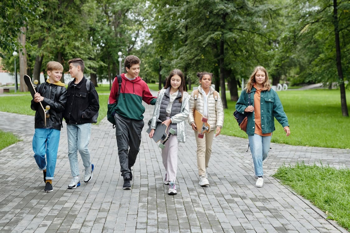 Free Group of teenagers walking and laughing together in a sunny park setting. Stock Photo