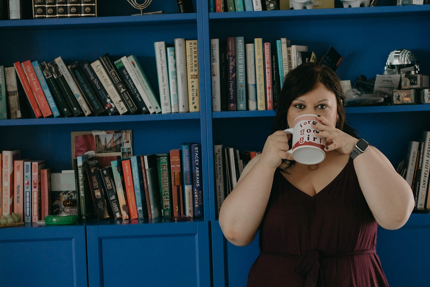 large blue bookshelf, chedva standing in front of it sipping coffee