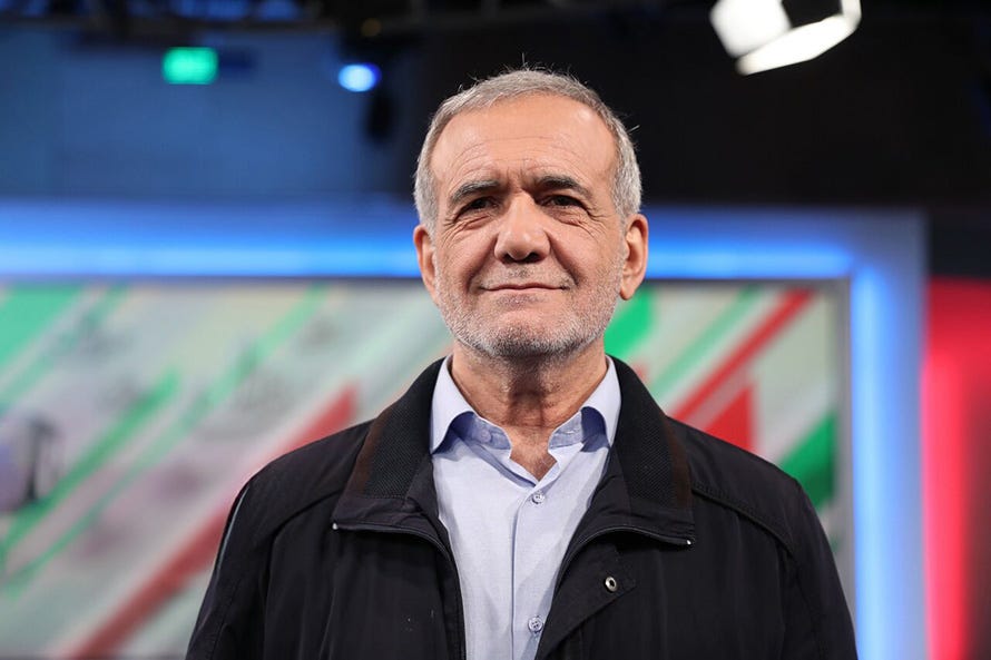 Iranian President Pezeshkian stands on a brightly lit TV stage, with a slight smile Iranian President Pezeshkian stands on a brightly lit TV stage, with a slight smile