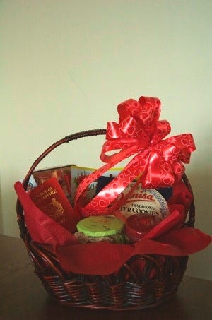 A gift basket with a large, red ribbon tied on the handle. It includes a large box of butter cookies and other various treats. A Singapore passport is placed among the snacks.