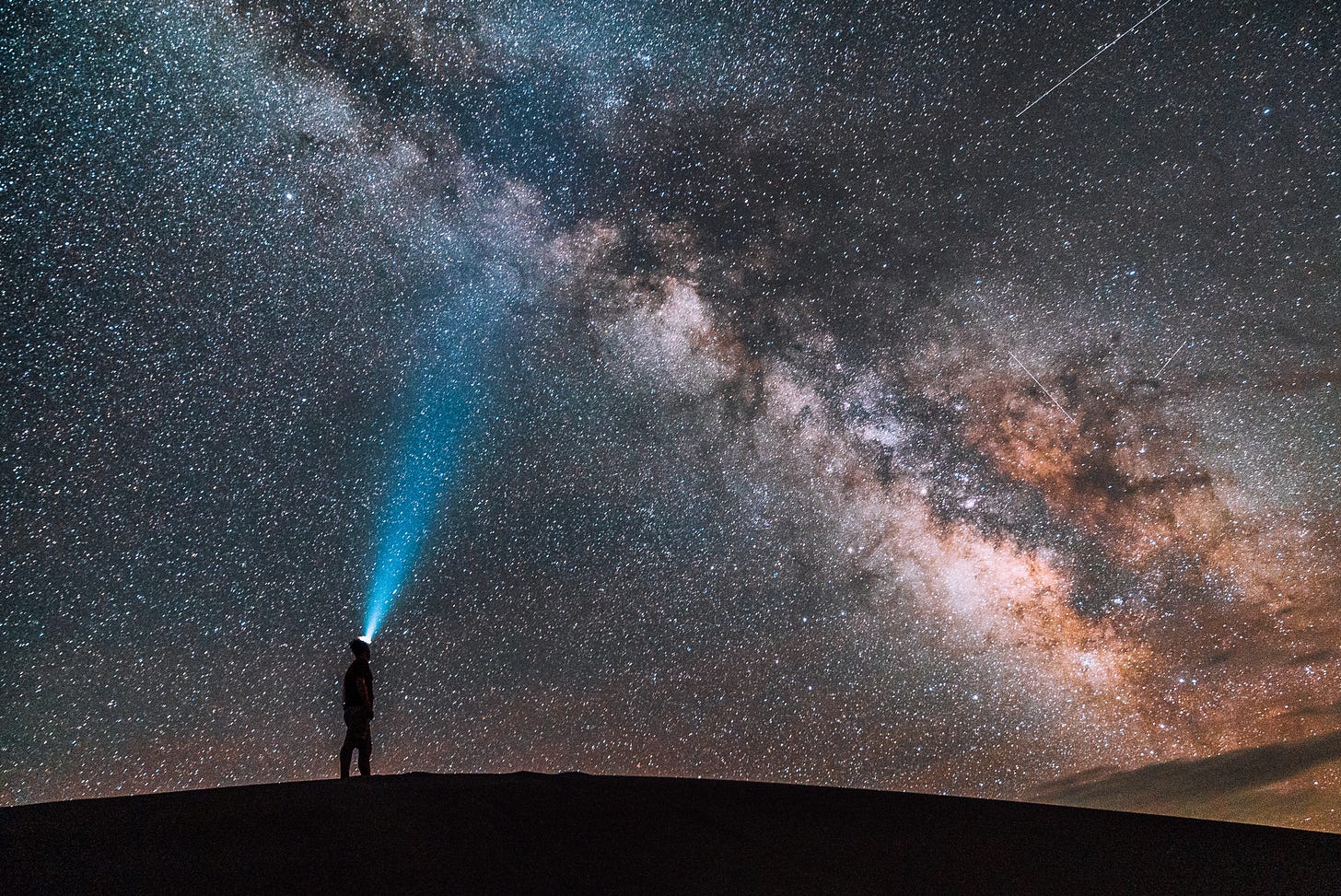 the milky way galaxy being illuminated by a figure with a headtorch the milky way galaxy being illuminated by a figure with a headtorch