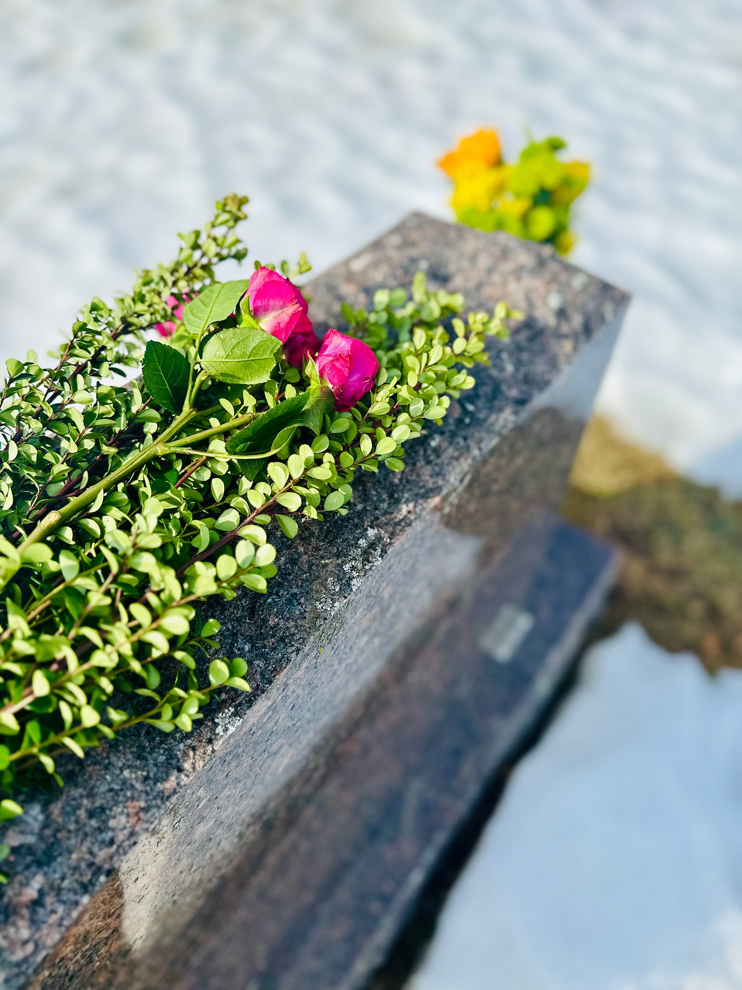 Gravestone with pink flowers & greenery on top and yellow flowers in the attached vase.