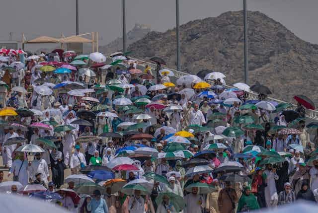 A large number of people holding umbrellas to shield themselves from the sun, with a bare mountain range in the background. A large number of people holding umbrellas to shield themselves from the sun, with a bare mountain range in the background.