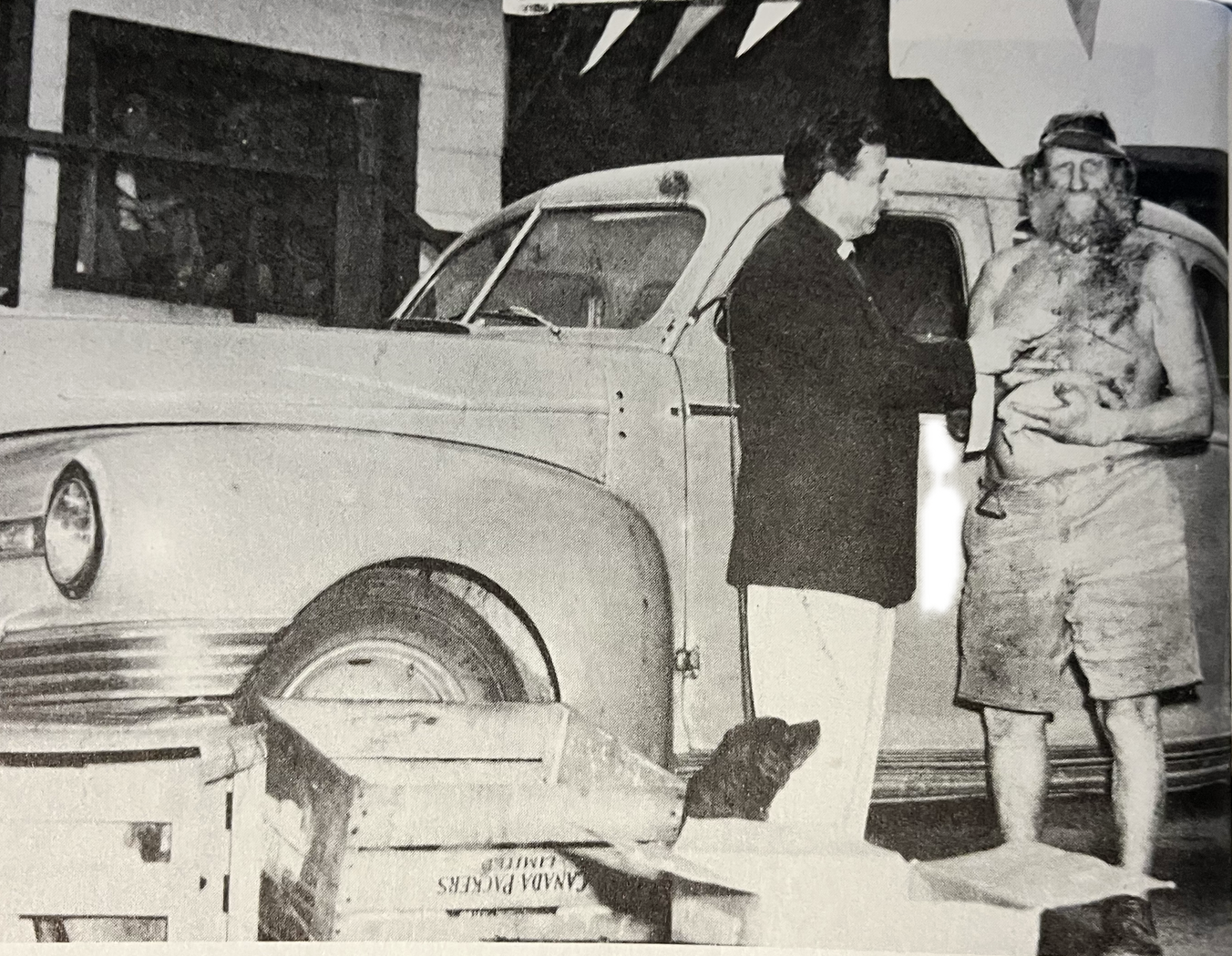 Black-and-white photograph of Willie Willey standing bare-chested in shorts beside a suited man in front of a late-1940s automobile at a Spokane dealership. The man appears to be presenting Willey with the car, which was given to him as a publicity replacement shortly before his fatal crash in 1956.
