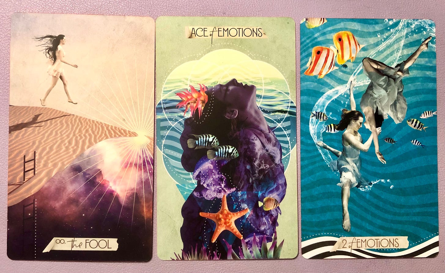 Three tarot cards displayed side by side: The Fool card showing a silhouetted figure walking across desert dunes toward a bright light, Ace of Emotions featuring a large purple crystal or geode with coral and sea life elements, and Two of Emotions depicting figures swimming underwater with whales and tropical fish.