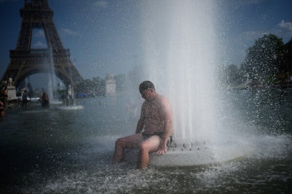A person cools off at Trocadero fountain near the Eiffel Tower during a heat wave in Paris, on June 24, 2026. (AP Photo/Christophe Ena, File)