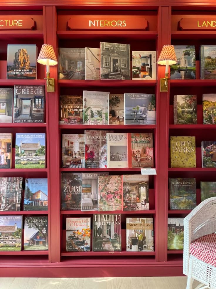 This may contain: a red book case filled with lots of books next to a white wicker chair