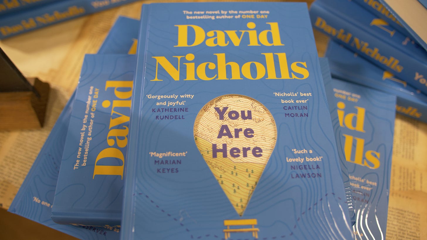 A close-up of several copies of You Are Here piled up on a table.