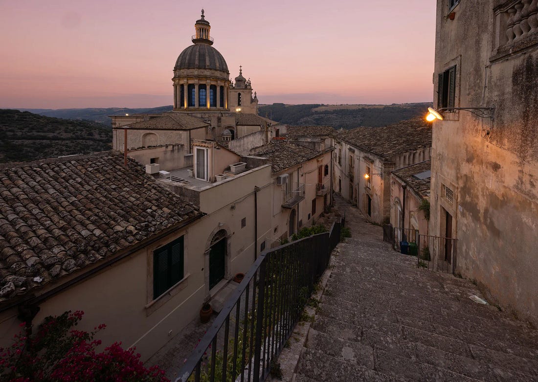 The dome of the Duomo di San Giorgio rising over the rooftops of Ragusa Ibla at dusk, with a stone stairway descending beside it. The dome of the Duomo di San Giorgio rising over the rooftops of Ragusa Ibla at dusk, with a stone stairway descending beside it.