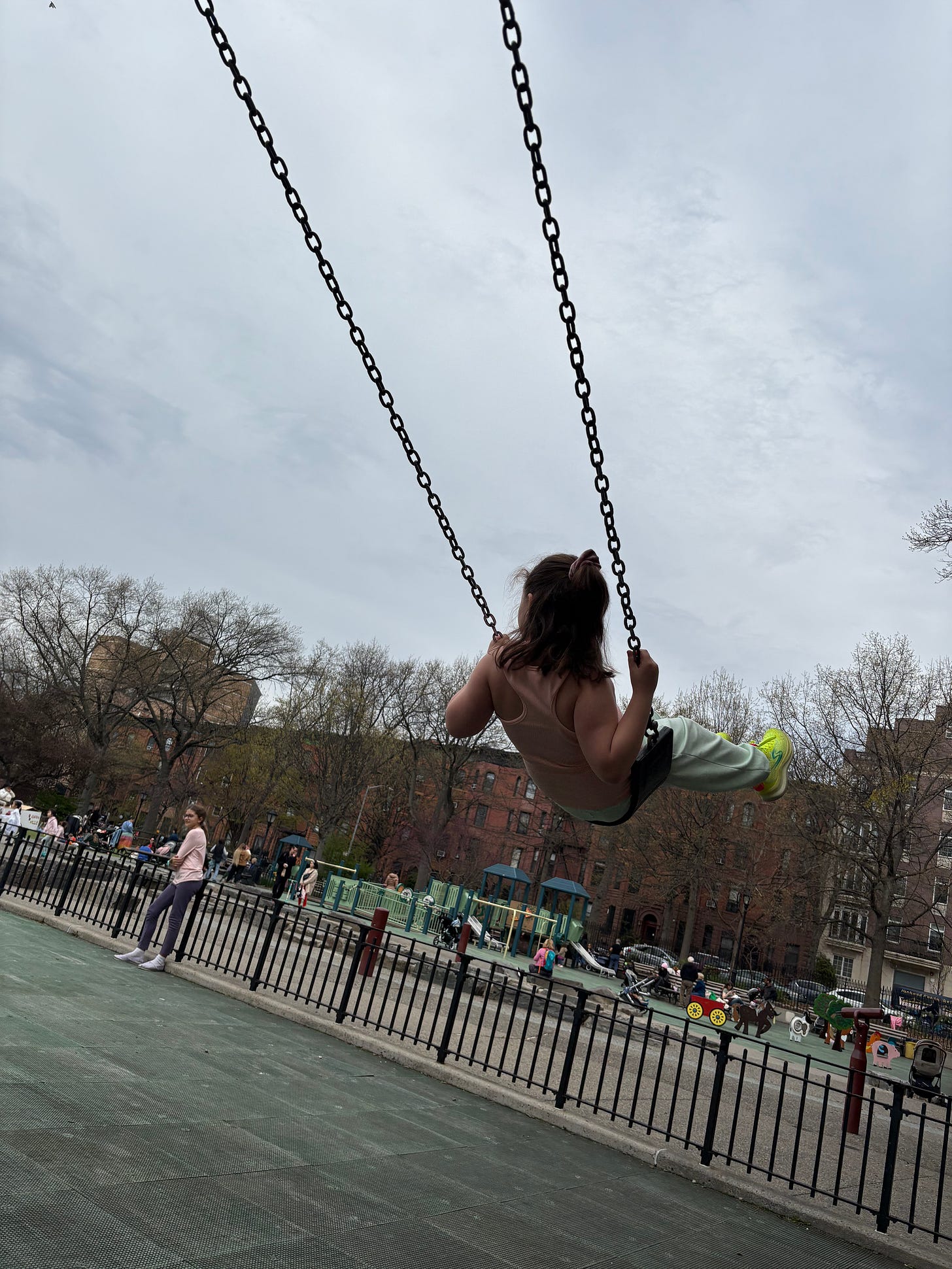 A girl in a tank top and sweatpants on a swing, silhouetted against a partly overcast sky.