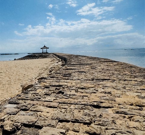An old cobbled road leading out to a pagoda in the ocean.