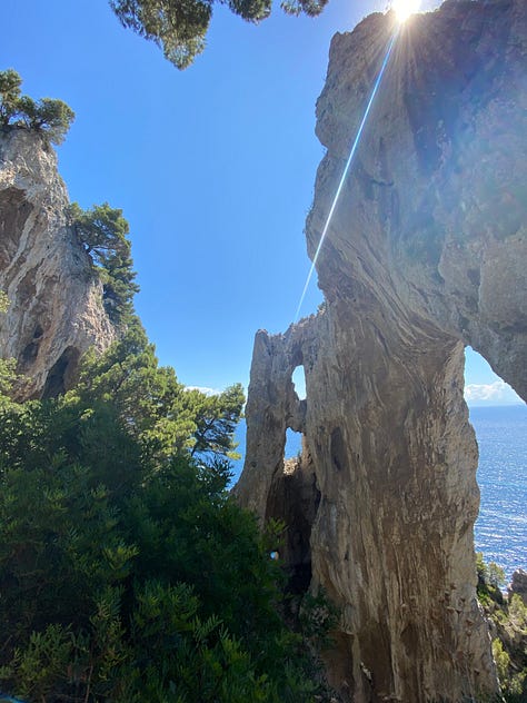 A gallery of three images of rock formations providing different views down to the Mediterranean Sea that surrounds the island of Capri. The rock formations provide different frames looking down from a high point on the island to the water below and the trees that line the images, peeking their green in. The sun shines from different angles in the different pictures.