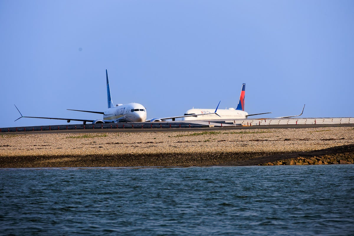 Two commercial airplanes on taxiway at Boston Logan Airport seen from Boston Harbor