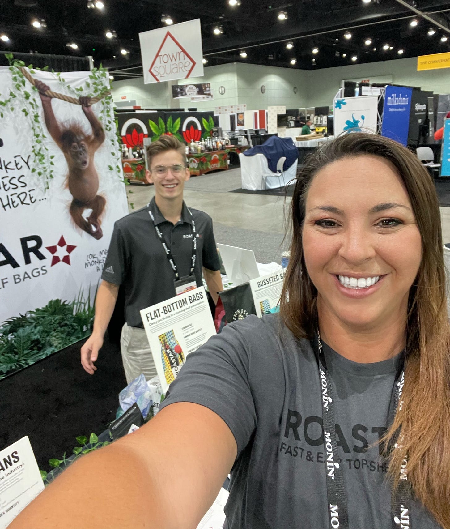 A woman takes a selfie in front of a convention booth in an arena. A woman takes a selfie in front of a convention booth in an arena.