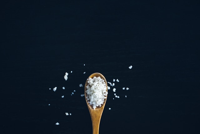 A wooden spoon filled with coarse salt, some of it spilling out onto a black background.