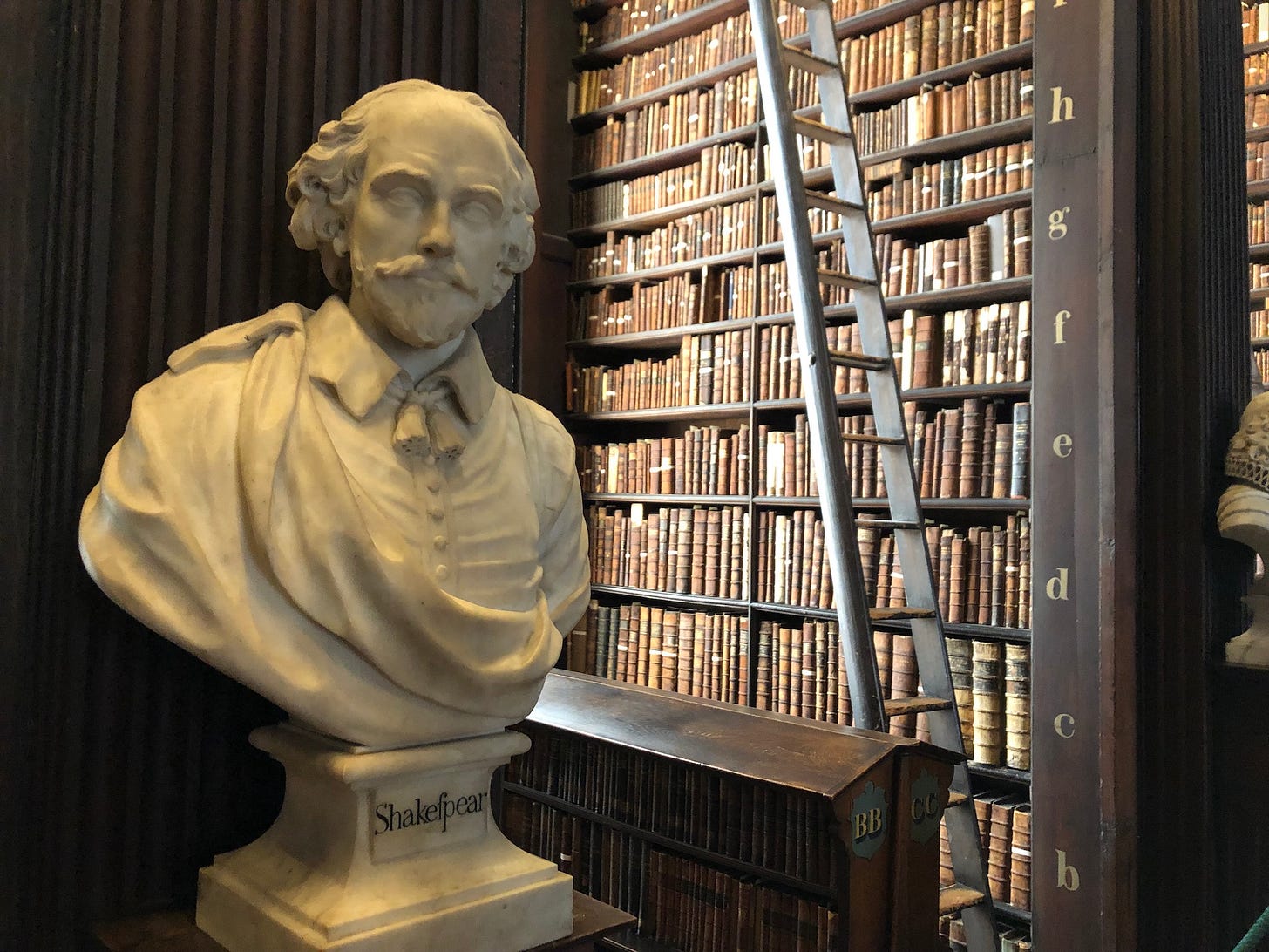 A bust of William Shakespeare in front of a column of brown books