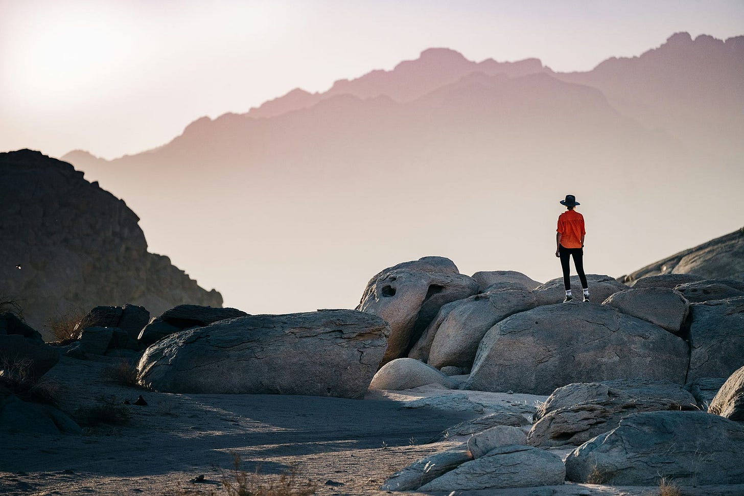 Photo of woman staring wistfully toward a towering mountain in the distance by NEOM on Unsplash