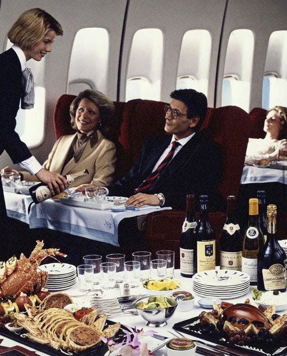 This may contain: an airplane dining area with people sitting at the table and eating food on the trays