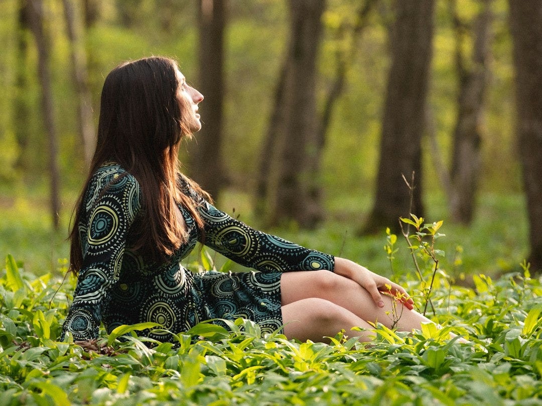 woman in black and white floral long sleeve dress sitting on green grass field during daytime