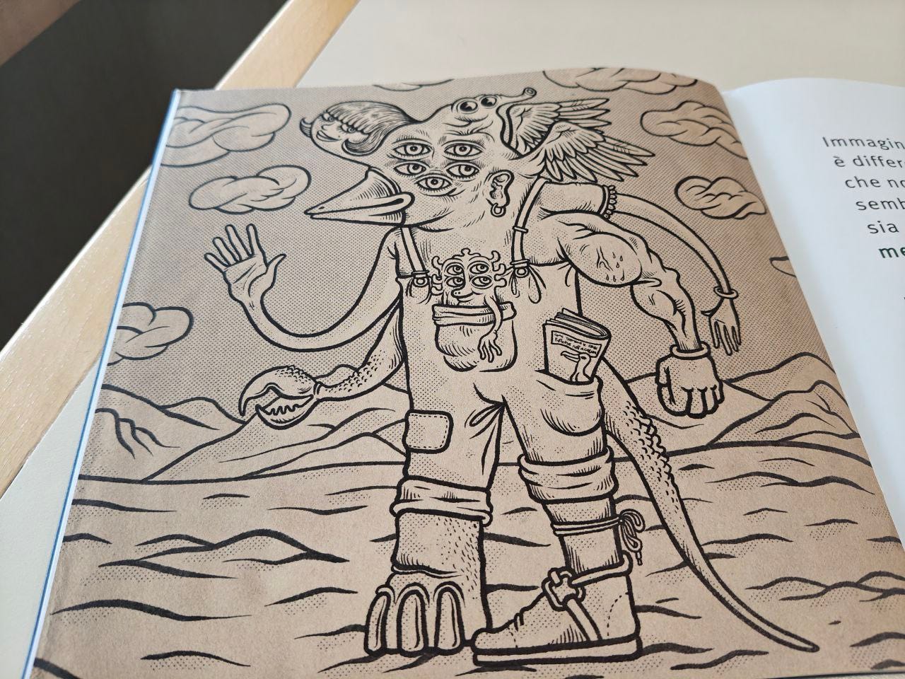 Pagina illustrata della Scatolina MOSTRO edita da effequ, appoggiata su un tavolo di legno color bianco sporco, con un pezzetto di muro in ombra nell'angolo in alto a sinistra. Nel disegno fatto con tono seppia e tecnica puntinata simile a quella dei dipinti di Roy Lichtenstein, compare un personaggio con quattro braccia sia umane, che animalesche, una testa che si disarticola in varie facce (di donna, con un becco, con cinque occhi, un orecchio, un altro muso da alieno con proboscide, due ali) e con due gambe, una delle quali è una zampa di elefante, più una cosa simile a quella dei dinosauri. Sullo sfondo un terreno desertico montuoso e nel cielo tante nuvole fluttuanti che assomigliano a pasta morbida.