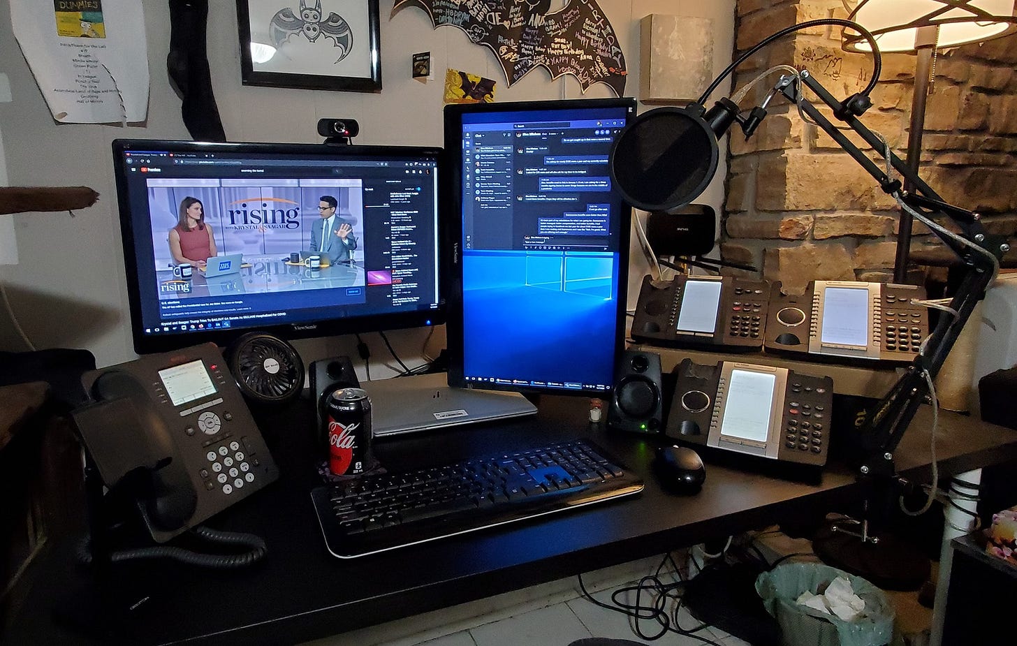 Computer desk with four phones, two monitors, and a USB microphone.