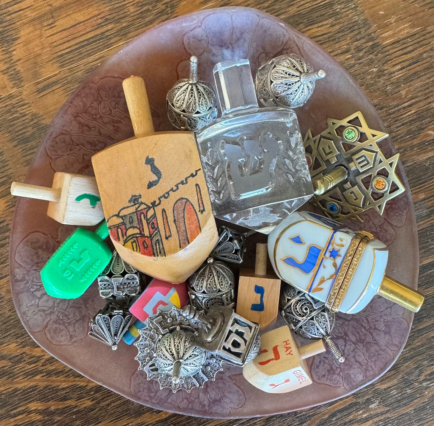 A group of dreidels in a glass bowl on a wood table.