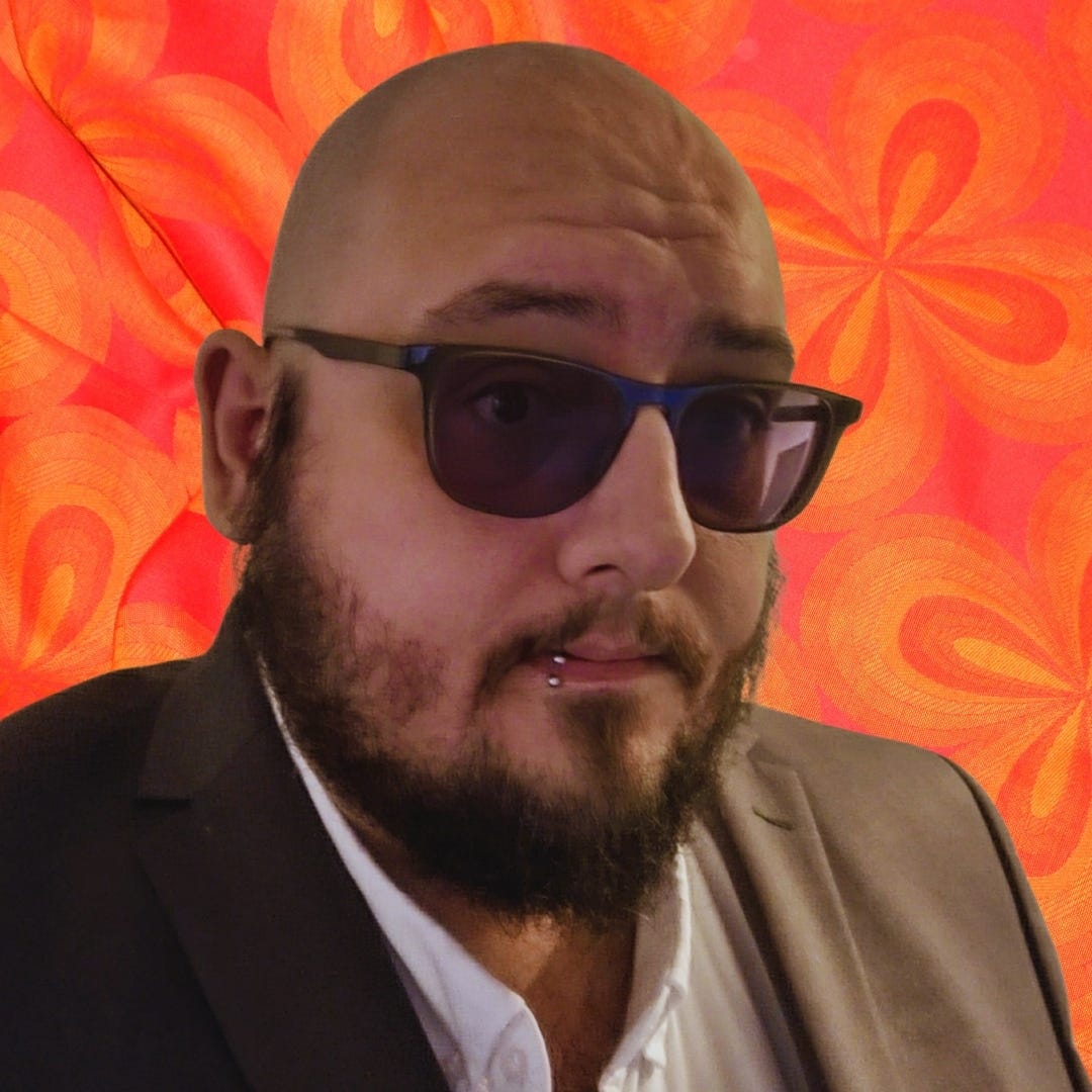 A headshot of David Gray-Hammond wearing a suit and sunglasses against an orange patterned background.